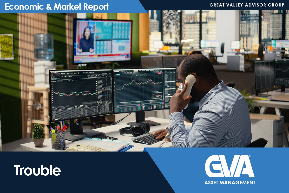Man at a trading desk on a phone, looking at multiple monitors displaying stock charts in a busy office with visible branding banners above and below.